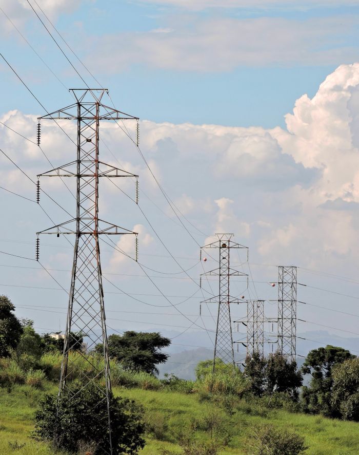 Electric pylons in a green landscape under a cloudy sky, showcasing rural energy infrastructure.